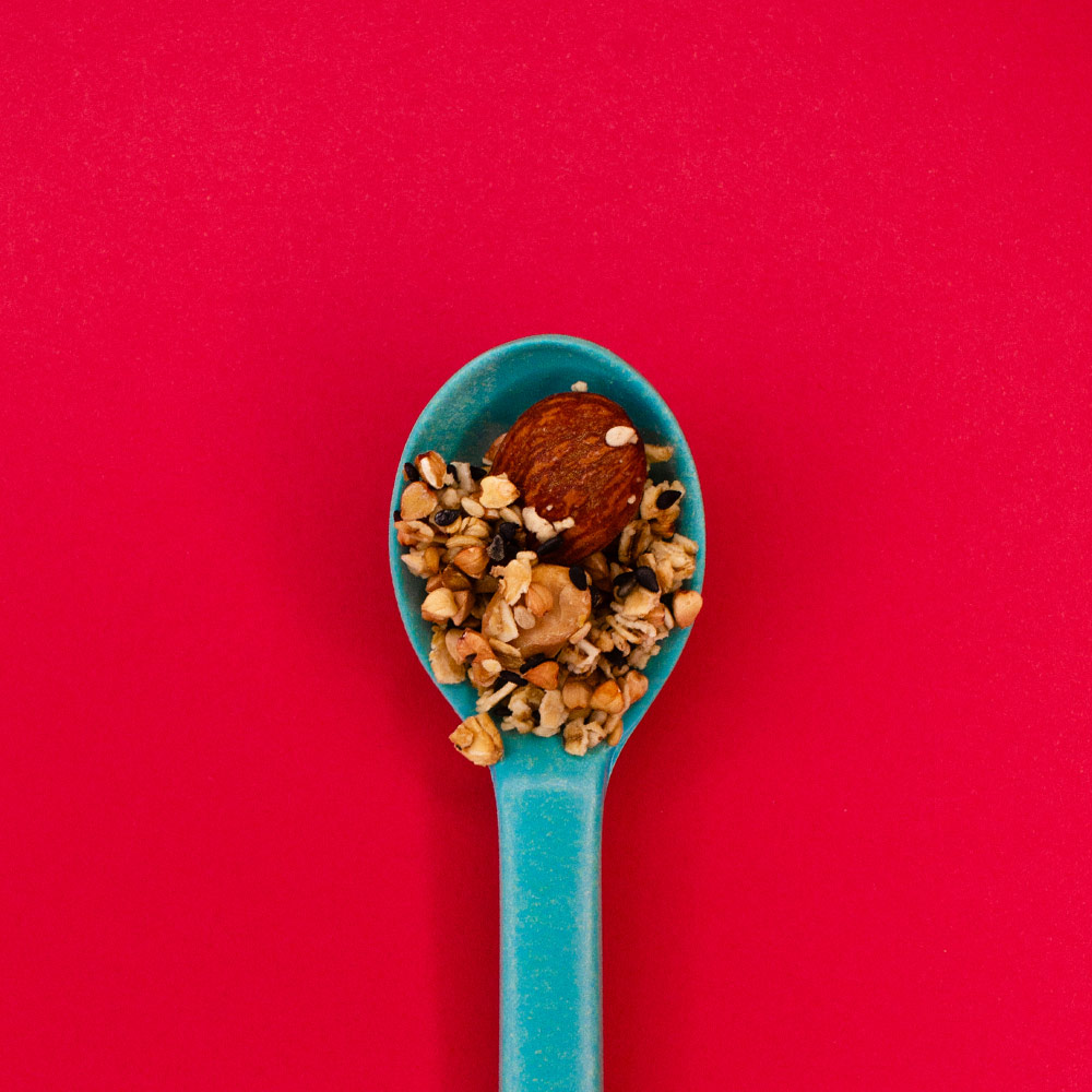 Une cuiller bleue remplie de granola sur fond rouge